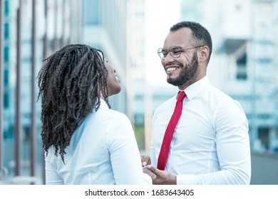 Happy Diverse Couple Chatting Outside. Business Man And Woman Standing In City Street, Holding Hands, Smiling And Talking. Corporate Relationship Concept