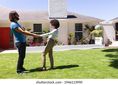 Happy Diverse Couple Dancing In Front Of House On Sunny Garden Terrace. Staying At Home In Isolation During Quarantine Lockdown.