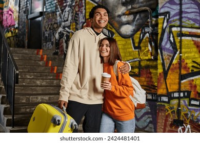 happy diverse couple embracing by a staircase with graffiti on background, black man with luggage - Powered by Shutterstock