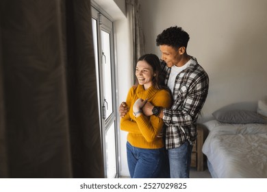 Happy diverse couple embracing and looking through window in bedroom at home, copy space. Expression, leisure, love, togetherness and domestic life unaltered. - Powered by Shutterstock