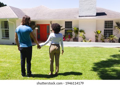 Happy Diverse Couple Holding Hands In Front Of House On Sunny Garden Terrace. Staying At Home In Isolation During Quarantine Lockdown.