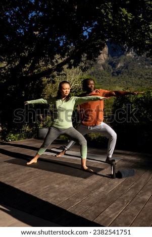 Happy diverse couple practicing yoga standing on deck in sunny garden, copy space. Yoga, fitness, togetherness, free time, relaxation, nature and heathy lifestyle, unaltered.