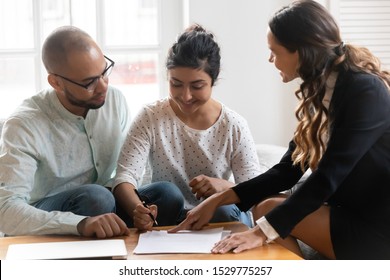 Happy diverse couple satisfied clients making deal, Indian wife signing contract at meeting after successful negotiation with realtor, mortgage insurance broker, family purchasing new apartment