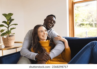 Happy diverse couple sitting on sofa embracing and smiling at home. Lifestyle, togetherness, relationship and dometic life, unaltered. - Powered by Shutterstock