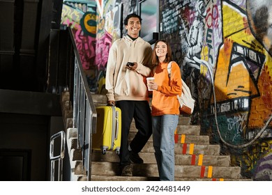 happy diverse couple standing on stairs with graffiti on wall, black man holding a yellow suitcase - Powered by Shutterstock