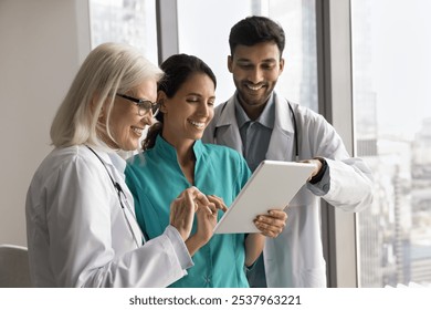 Happy diverse doctors workmates use tablet pc for medical service enjoy easy work with electronic documentation in smart online app. International clinic staff group talk consult discuss patient case - Powered by Shutterstock