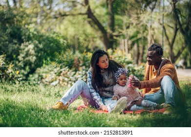 Happy Diverse Family Of Three Spending Their Free Time In The Park And Enjoying Beautiful Sunny Day Outside. Multiracial Parents And Their Cute Little Daughter Having Fun Together.