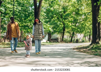 Happy Diverse Family Of Three Spending Their Free Time In The Park And Enjoying Beautiful Sunny Day Outside. Multiracial Parents And Their Cute Little Daughter Having Fun Together.