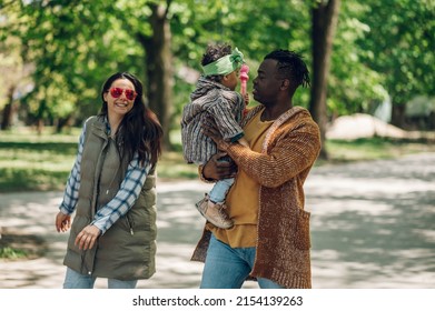 Happy Diverse Family Of Three Spending Their Free Time In The Park And Enjoying Beautiful Sunny Day Outside. Multiracial Parents And Their Cute Little Daughter Having Fun Together.