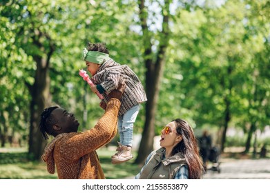 Happy Diverse Family Of Three Spending Their Free Time In The Park And Enjoying Beautiful Sunny Day Outside. Multiracial Parents And Their Cute Little Daughter Having Fun Together.