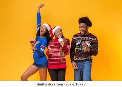 Happy diverse friends in Christmas sweaters drinking, singing, celebrating and having fun together in yellow isolated background studio shot - Powered by Shutterstock