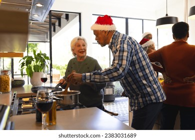 Happy diverse friends couple in santa hat preparing food in sunny kitchen at home. Retirement, friendship, christmas, celebration cooking, eat, senior lifestyle, unaltered. - Powered by Shutterstock