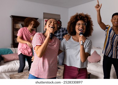 Happy diverse friends dancing and karaoke singing with microphone at home. Domestic life, friendship, music and lifestyle, unaltered. - Powered by Shutterstock