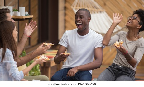 Happy diverse friends listening to young man telling funny story making laugh sharing dinner, multi-ethnic students people eat pizza in cafe terrace outdoor talking having fun together at meeting