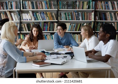 Happy Diverse Group Of College Students Working Together On Study Project In University Library, Sitting At Table With Books, Laptop, Talking Discussing Research, Learning Tasks, Laughing