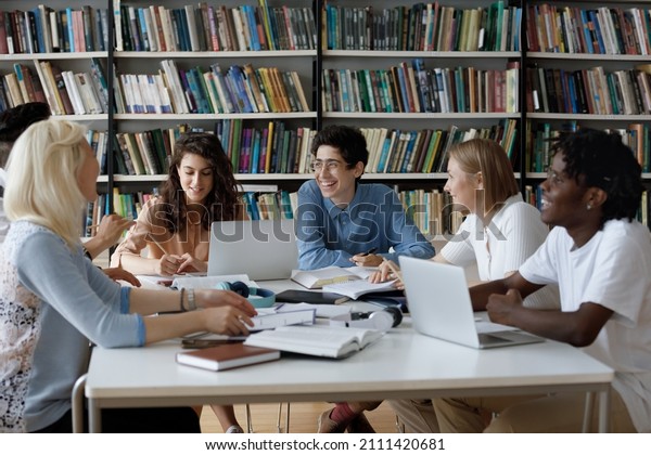 Happy\
diverse group of college students working together on study project\
in university library, sitting at table with books, laptop, talking\
discussing research, learning tasks,\
laughing