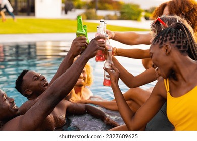 Happy diverse group of friends having pool party, drinking beer and making a toast in garden. Lifestyle, friendship and party, summer, sunshine, unaltered.