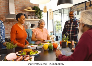 Happy diverse group of senior friends preparing meal in sunny kitchen at home. Retirement, friendship, cooking, eat, togetherness and senior lifestyle, unaltered. - Powered by Shutterstock