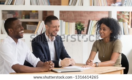 Happy diverse hr managers laughing at funny joke listen to african female applicant at job interview, winning black candidate make good positive first impression on recruiters during hiring process