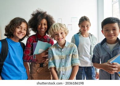 Happy diverse junior school students children group looking at camera standing in classroom  Smiling multiethnic cool kids boys   girls friends posing for group portrait together 