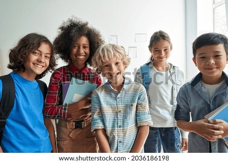 Happy diverse junior school students children group looking at camera standing in classroom. Smiling multiethnic cool kids boys and girls friends posing for group portrait together.