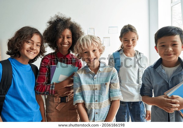 Happy diverse\
junior school students children group looking at camera standing in\
classroom. Smiling multiethnic cool kids boys and girls friends\
posing for group portrait\
together.