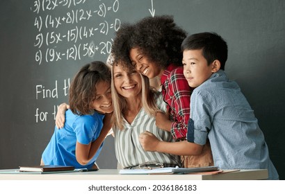 Happy diverse kids, multicultural junior school children students hugging embracing female teacher appreciating and thanking educator in classroom, having fun, celebrating back to school concept.