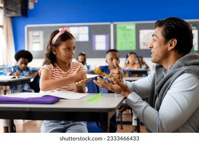 Happy diverse male teacher teaching girl using sign language in elementary school class. School, learning, childhood, disability, teaching and education, unaltered. - Powered by Shutterstock