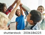 Happy diverse multiethnic kids junior school students group giving high five together in classroom. Excited children celebrating achievements, teamwork, diversity and friendship with highfive concept.