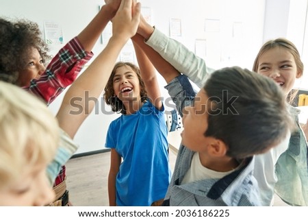 Happy diverse multiethnic kids junior school students group giving high five together in classroom. Excited children celebrating achievements, teamwork, diversity and friendship with highfive concept.