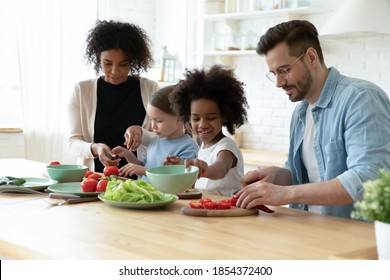 Happy diverse parents with adorable daughters preparing meal together, African American mother and Caucasian father with two little kids cooking salad, multiracial family enjoying leisure time - Powered by Shutterstock