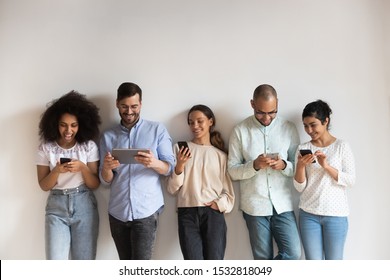 Happy diverse people using electronic devices, smartphones and tablet, standing in row on grey background, chatting in social network online, playing mobile phone games, having fun, shopping - Powered by Shutterstock