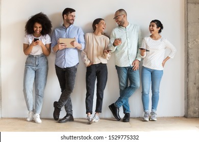Happy diverse people using phones, laughing at funny video, having fun together, standing in row against gray wall, chatting in social network online, playing mobile phone games, shopping