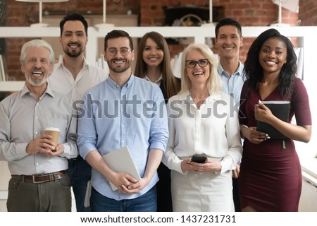 Happy diverse professional business team stand in office looking at camera, smiling young and old multiracial workers staff group pose together as human resource, corporate equality concept, portrait