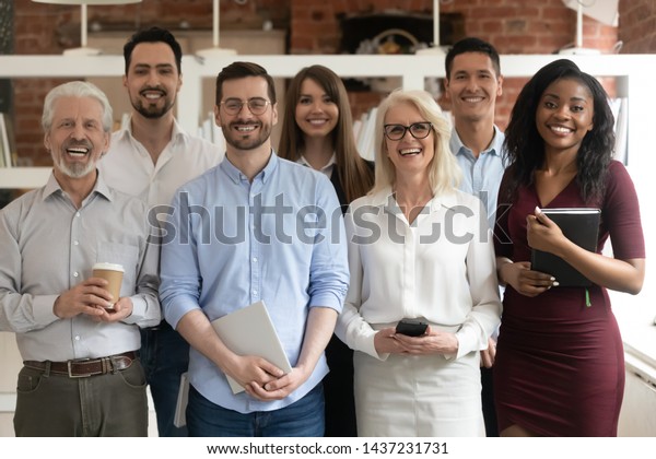 Happy diverse professional business team stand\
in office looking at camera, smiling young and old multiracial\
workers staff group pose together as human resource, corporate\
equality concept,\
portrait