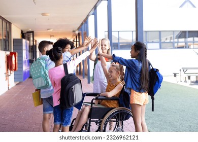 Happy diverse school children high fiving with girl in wheelchair in school corridor, copy space. Education, inclusivity, elementary school and learning concept. - Powered by Shutterstock