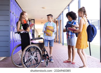 Happy diverse school children talking with girl in wheelchair in school corridor copy space. Education, inclusivity, elementary school and learning concept. - Powered by Shutterstock