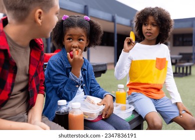 Happy diverse schoolchildren sitting at table and eating lunch at school. Education, inclusivity, elementary school and learning concept. - Powered by Shutterstock