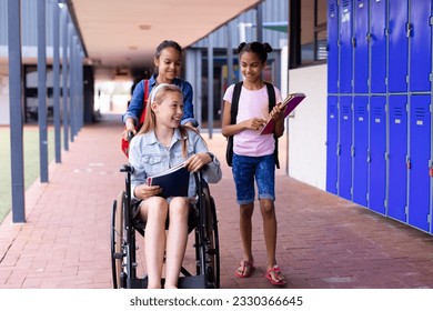 Happy diverse schoolgirl in wheelchair with her friends in corridor at school. Education, inclusivity, school, learning and disability concept. - Powered by Shutterstock