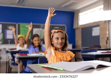 Happy diverse schoolgirls sitting at desks and raising hands in classroom. School, study and education, unaltered. - Powered by Shutterstock