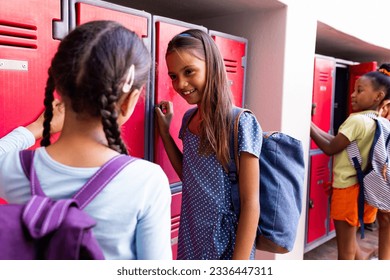 Happy diverse schoolgirls wearing school bags and talking at school lockers. School, study and education, unaltered. - Powered by Shutterstock