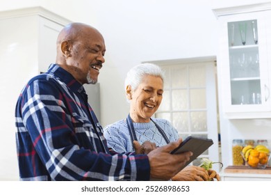 Happy diverse senior couple preparing meal using tablet in kitchen. Lifestyle, retirement, senior lifestyle, food, cooking, togetherness, communication, recipe and domestic life, unaltered. - Powered by Shutterstock