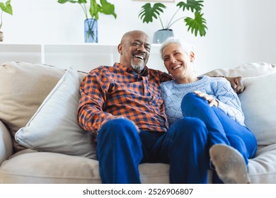 Happy diverse senior couple sitting on sofa and embracing in sunny living room. Lifestyle, retirement, senior lifestyle, togetherness and domestic life, unaltered. - Powered by Shutterstock