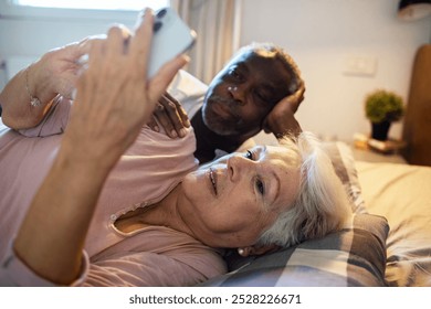 Happy diverse senior couple taking selfie in bed at home - Powered by Shutterstock