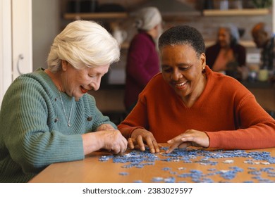 Happy diverse senior female friends playing with jigsaw puzzles in sunny dining room at home. Retirement, friendship, wellbeing, activities, togetherness and senior lifestyle, unaltered. - Powered by Shutterstock