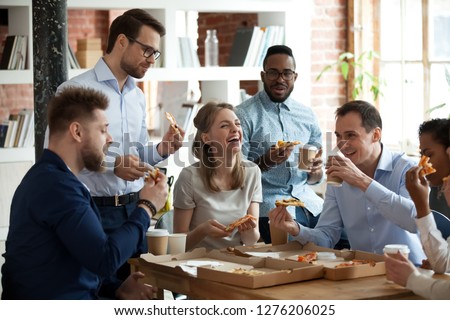 Happy diverse team people talking laughing at funny joke eating ordered pizza in office, friendly employees group enjoy positive emotions sharing lunch together having fun at work break on friday