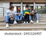 Happy diverse university student friends doing homework together sitting on campus steps. Higher education and technology concept.