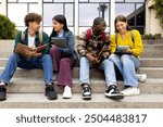 Happy diverse university student friends doing homework together sitting on campus steps. Higher education and technology concept.