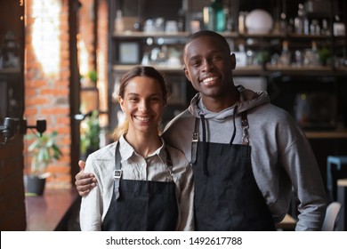 Happy diverse waiter and waitress looking at camera, smiling african male mixed race female two cafe colleagues stand in restaurant, millennial business team wear apron posing in coffee shop portrait - Powered by Shutterstock