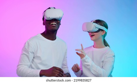 Happy Diverse Young People In White Clothes And Helmet Isolated Over Neon Background. African-American Man And Caucasian Woman Testing Ar Goggles